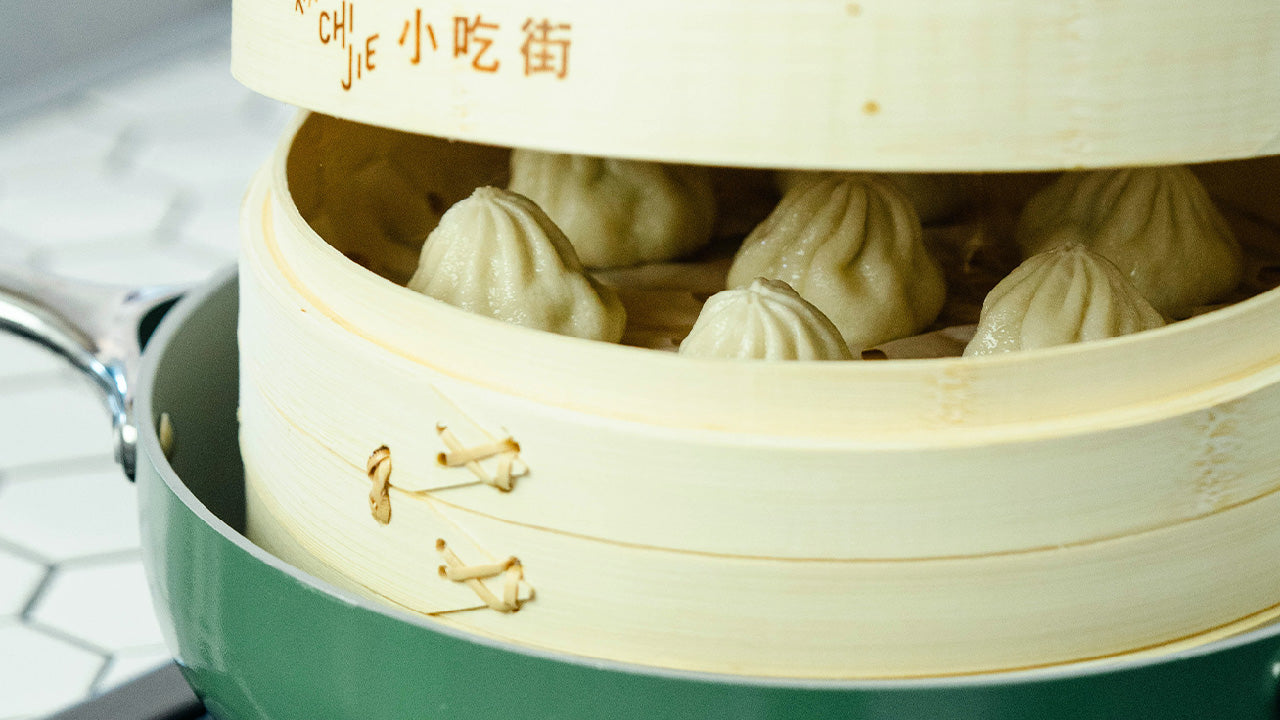 Soup dumplings steaming in a bamboo steamer set over a green pot
