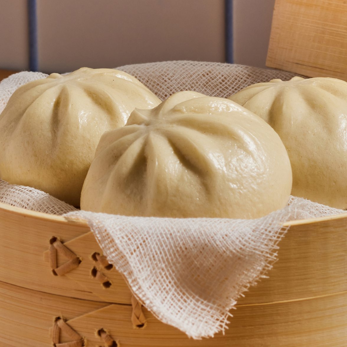 Close up of Chinese BBQ flavored pork bao buns showing pleated steamed tops in a bamboo steamer lined with cloth