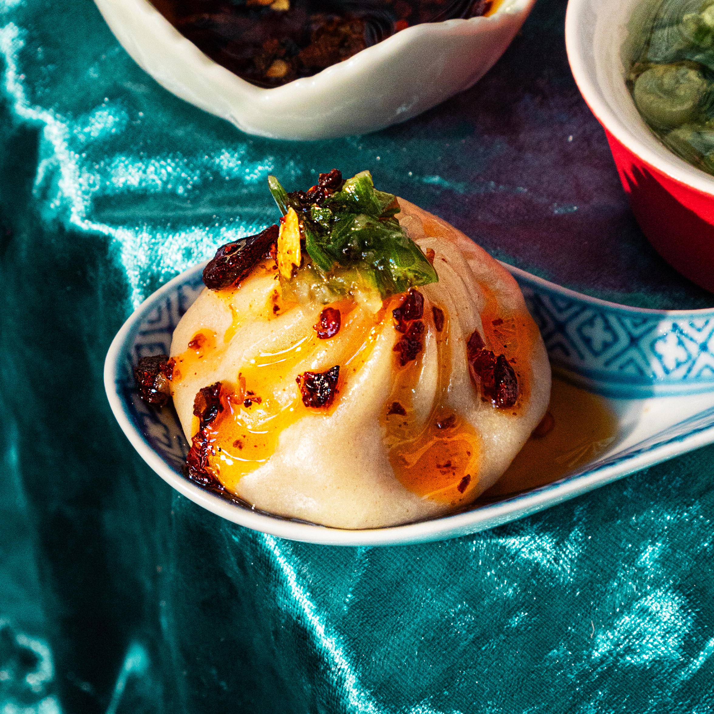 Pork soup dumplings topped with chili crisp and herbs on a plate