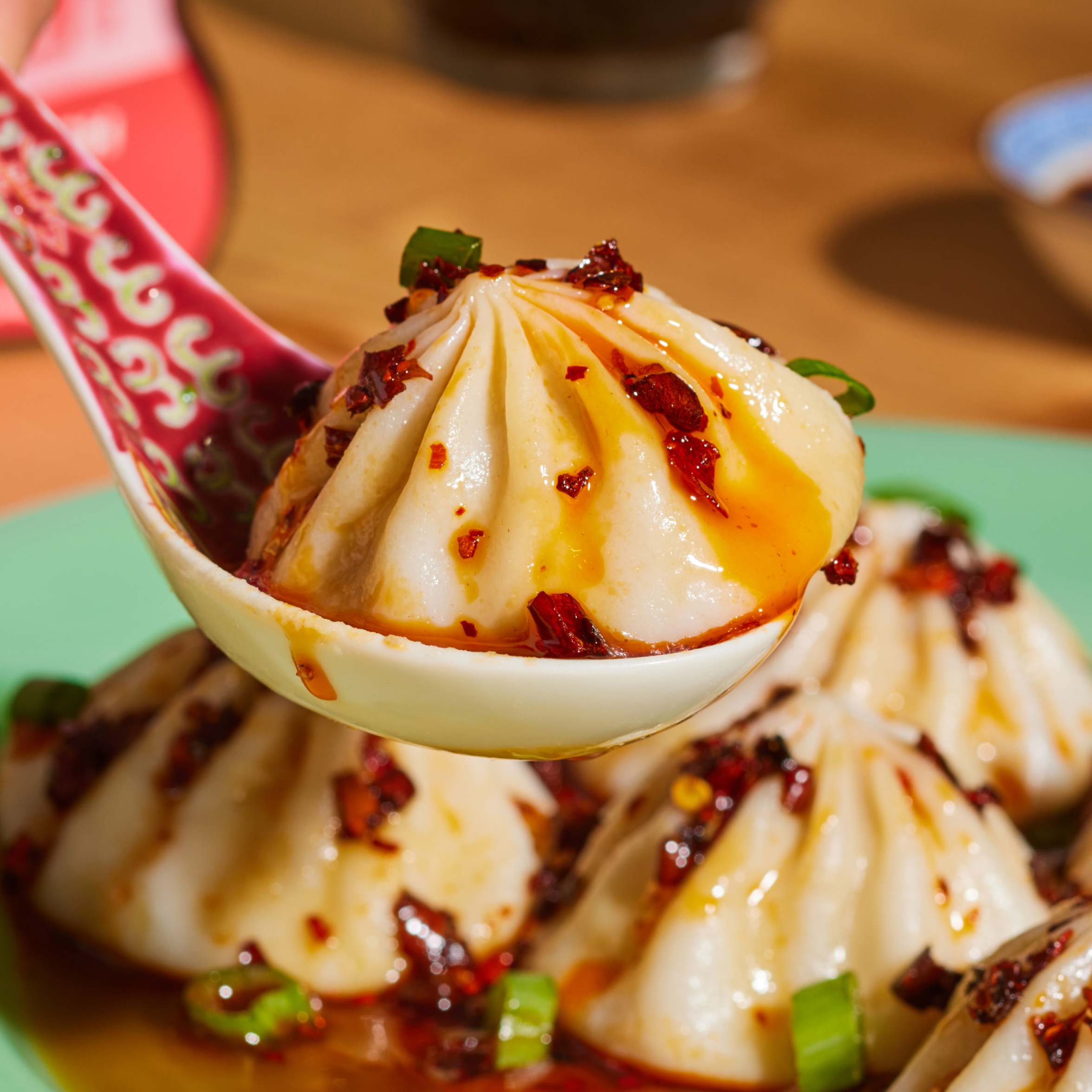 Close-up of Microwave Pork Soup Dumplings showcasing pleated wrappers and chili oil with more dumplings blurred behind