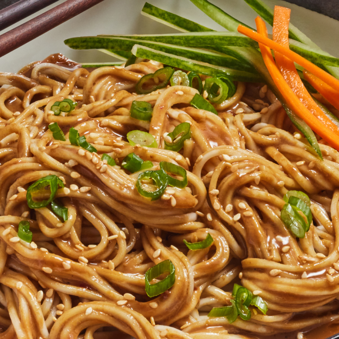 Close-up of Creamy Sesame Noodle showcasing wheat noodles coated in creamy sesame sauce with sesame seeds, scallions, cucumber and carrot garnish