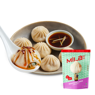 Three-quarter view of MìLà chicken soup dumplings showcasing a soup-filled dumpling on a porcelain spoon with dipping sauce and product pouch