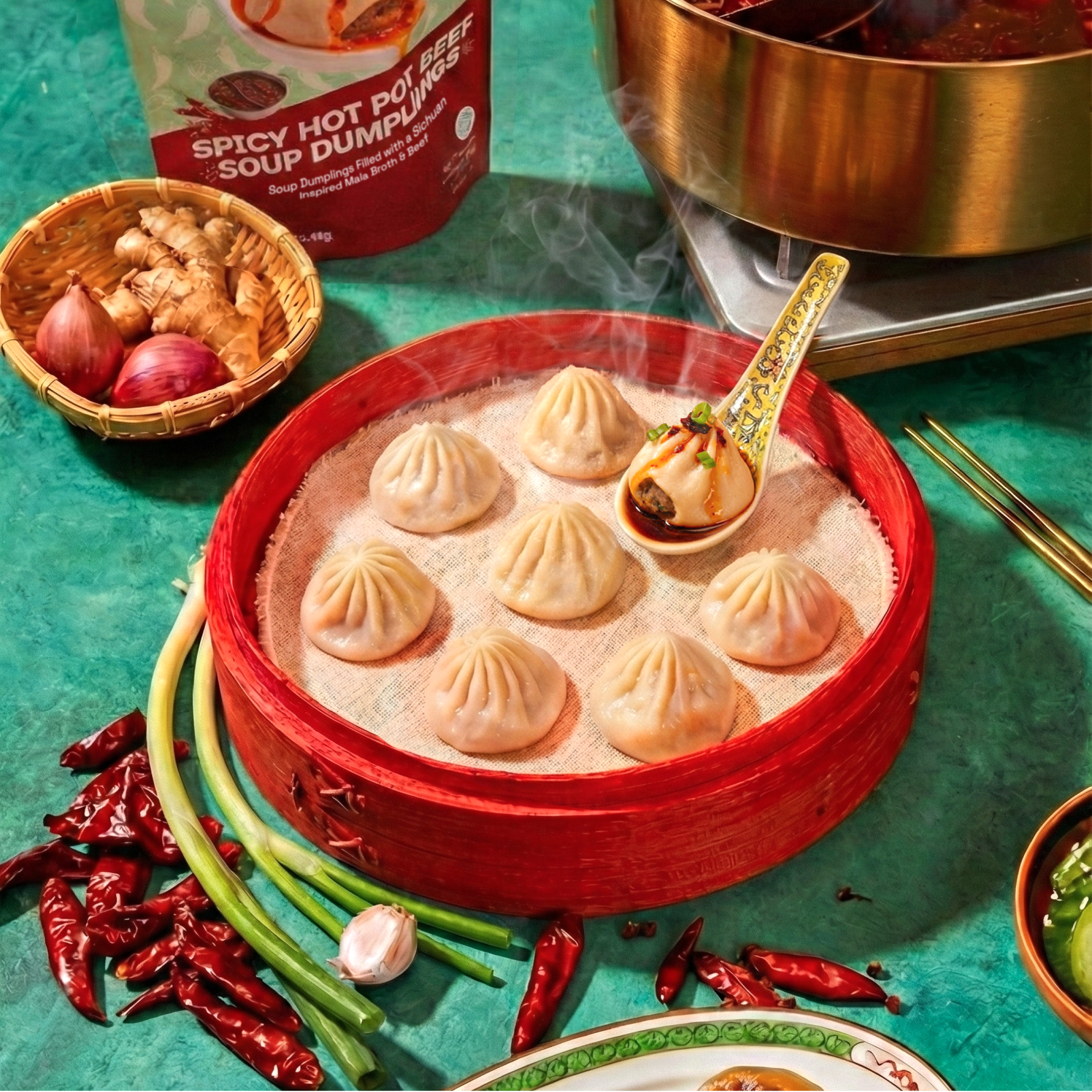 Steaming Spicy Hot Pot Beef soup dumplings in a red bamboo steamer with a sauced dumpling on a spoon and product box behind