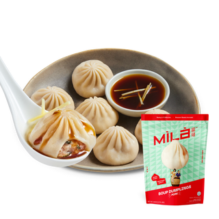 Front view of MìLà Classic Pork Soup Dumplings box with steamed soup dumplings on a plate and dipping sauce on white background