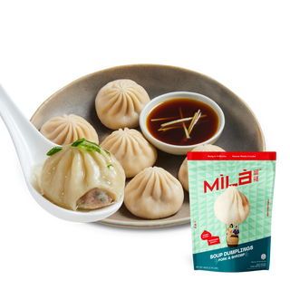 Close up of MìLà pork and shrimp soup dumplings, one on a spoon showing soupy filling, with dipping sauce and product pouch